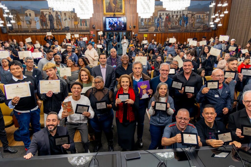 No dia 15 de agosto, o Salão Nobre do Palácio Anchieta, sede da Câmara Municipal de São Paulo, foi palco da 26ª edição do “Dia da Liderança Jovem”, um evento que tem como objetivo reconhecer e valorizar o protagonismo dos jovens paulistanos e os trabalhos voltados ao amadurecimento pessoal e social dessa parcela da população. A cerimônia também marcou a celebração dos 18 anos da Associação São Paulo Diferenciado, entidade que atua no desenvolvimento de unidades habitacionais de interesse social. O encontro, que reuniu estudantes, educadores, representantes da sociedade civil e autoridades, contou com o apoio da vereadora dra. Sandra Tadeu (PL), que destacou a importância de estimular o engajamento dos jovens e promover o contato deles com a política. “Isso é muito importante, a gente estimula o aluno, estimula o jovem. O jovem tem que saber a importância que ele tem, o nosso futuro. A gente já tá indo para trás, eles estão vindo para frente e eles têm que perceber o quanto é importante esse preparo, esses movimentos, participar em uma casa como a Câmara Municipal de São Paulo. Então, eu tô muito feliz”, afirmou a parlamentar. Homenagens e reconhecimentos Durante a solenidade, diversas personalidades foram homenageadas pelo trabalho desenvolvido em prol da juventude. Um dos destaques foi Edilson Venturelli, CEO do Instituto Baccarelli, organização reconhecida pelo trabalho cultural e educacional realizado na comunidade de Heliópolis. “Eu fico muito feliz e agradecido pela vereadora Sandra Tadeu por mais esse reconhecimento. O Baccarelli trabalha há mais de 29 anos promovendo justamente o protagonismo da Juventude. Então, estar na Câmara, que representa a população de São Paulo, tendo esse trabalho reconhecido, é sempre uma questão de honra e de muita emoção”, declarou Venturelli. O professor e publicitário Antônio Gelfusa Jr., que participou da primeira edição do Dia da Liderança Jovem sendo um dos primeiros contemplados pela premiação, também foi outro homenageado da noite. Com uma trajetória marcada pela dedicação à comunicação e à educação, o professor relembrou sua juventude e destacou a importância de eventos como este, para refletir sobre as políticas públicas e o incremento de oportunidades para os mais novos por parte dos governos: “Quando você é mais novo, você sempre se preocupa, ‘como vai ser meu futuro?’, ‘por quais caminhos eu vou percorrer?’. E é legal, a vida me levou para a área da publicidade, do jornalismo, para a área da docência. Então, hoje, eu trabalho com educação, com comunicação e o futuro me permitiu chegar até aqui. Passaram-se uns bons anos e eu acho que a data também ajuda a gente a pensar mais sobre o acesso de políticas públicas aos jovens, por meio de mais educação, cultura e outras questões de retaguarda que ajudam o jovem a estudar mais e melhor, como a mobilidade, a moradia, a saúde, a alimentação, dentre outros”, refletiu Gelfusa Jr. 18 anos da Associação São Paulo Diferenciado Além das homenagens, a cerimônia celebrou os 18 anos da Associação São Paulo Diferenciado, organização que tem atuado em projetos de habitação social na capital. Em seu discurso, o presidente da entidade, professor Emerson Nunes de Oliveira, anunciou conquistas recentes e ressaltou a importância da parceria com o poder público. “Hoje, nós pré-selecionamos 62 famílias que vão morar no residencial que chama São Paulo Diferenciado, lá em Itaquera. Então, eu quero agradecer muito a vereadora Sandra Tadeu por essa oportunidade, por mais um ano junto com ela”, afirmou. Entre as famílias contempladas está Maria Cristina, que não escondeu a emoção ao falar sobre a conquista da moradia: “É gratificante, essa é a quarta ou quinta liderança que participo, e acho muito interessante em relação à moradia, muito gratificante. Eu não sou a única que será contemplada, mas, assim, hoje, são 62 famílias que dormem tranquilas com a certeza de que terão um teto para se abrigar e logo mais serão mais 60, 100 famílias, enfim. Não tenho palavras, só agradecer e dizer o quanto é gratificante de verdade viver esse momento”, disse emocionada. Com discursos emocionados, homenagens marcantes e anúncios importantes, o evento deixou claro que investir no jovem é investir no futuro. E, como destacou a vereadora Sandra Tadeu, é papel da sociedade como um todo “estimular o aluno, estimular o jovem”, pois é deles que dep